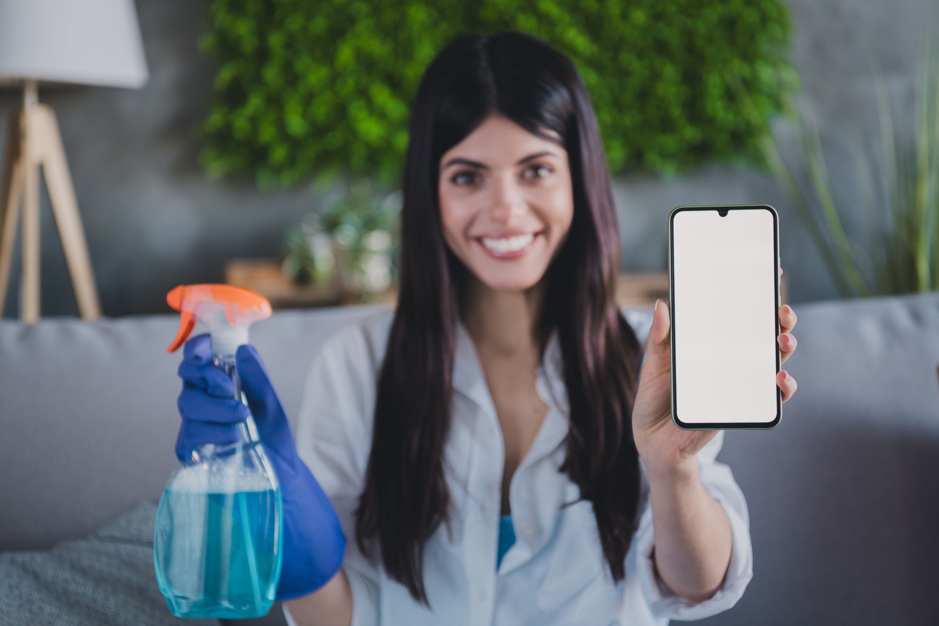 Woman smiling while displaying a phone screen and holding a cleaning spray indoors
